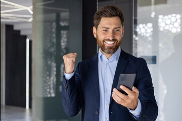 Successful businessman celebrating with smartphone in office