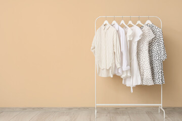 Stylish female clothes hanging on rack near color wall