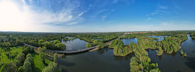 Sunny day aerial view of treelined lake, blue water, white clouds in sky Hanover Ricklinger Teiche...