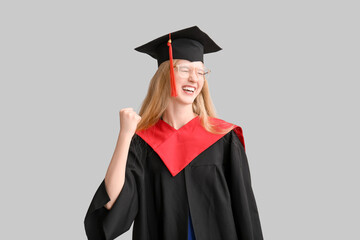 Happy female graduating student in mortar board on grey background