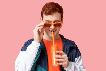 Young man in sunglasses drinking soda on pink background