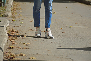 slender female legs in blue jeans and sneakers. light and comfortable shoes and clothing for work, leisure and everyday walks in the fresh air