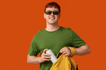 Young man with can of soda in his backpack on orange background