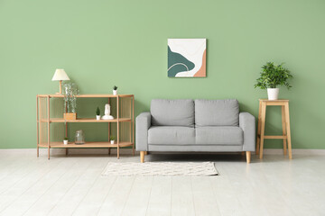 Modern living room with wooden shelving unit and grey sofa near green wall