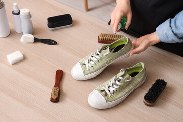 Female shoemaker with stylish gumshoes and cleaning supplies at wooden table