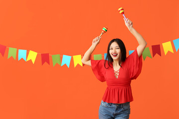 Happy young woman with maracas and festive garland on orange background