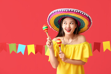Happy young woman in Mexican sombrero hat and with maracas on red background