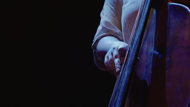 A man playing a contrabass with his hand in slow motion. Concept of calm and focus as the musician plays his instrument