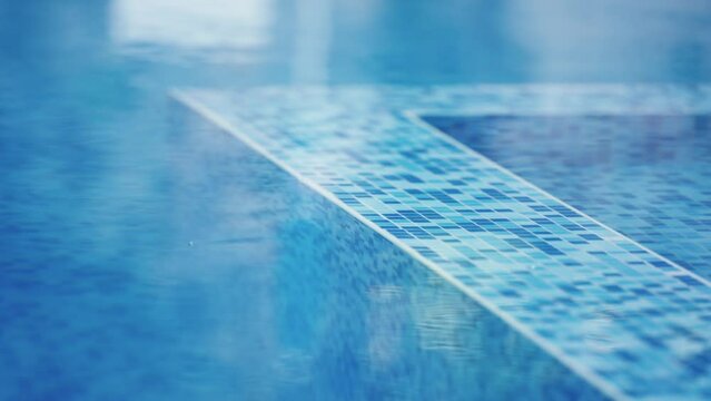A blue tile pool edge with a reflection of the pool in the water. The tiles are blue and white