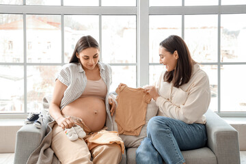 Young pregnant lesbian couple with baby clothes sitting on sofa at home