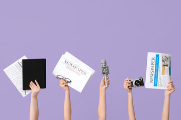 Female hands with newspapers, photo camera, notebook and microphone on lilac background