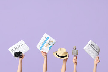 Female hands with newspapers, hat, microphone and photo camera on lilac background