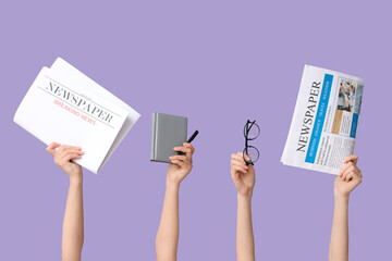 Female hands with newspapers, notebook and eyeglasses on lilac background