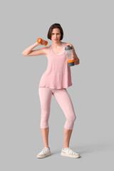 Beautiful young woman with bottle of water and dumbbell on grey background. Weight loss concept