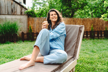 One young caucasian woman is relaxing on easy bed while drinking cold coffee in her backyard