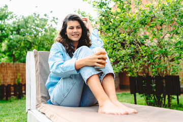 Naklejka premium One young caucasian woman is relaxing on easy bed while drinking cold coffee in her backyard