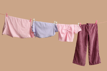 Different clothes hanging on rope against color background