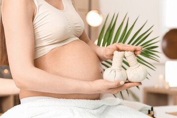 Young pregnant woman with herbal bags in spa salon, closeup