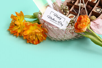 Basket with candies, bottle of wine and tulip flowers for Mother's Day celebration on color background