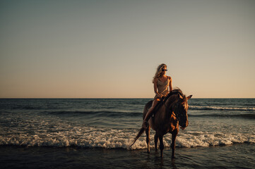 Front portrait of a woman riding a horse on a beach during a sunset