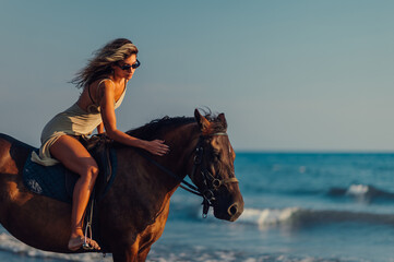 Woman petting her horse while riding it on a sea or ocean beach
