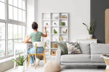 Young woman turning on air conditioner at table in living room, back view