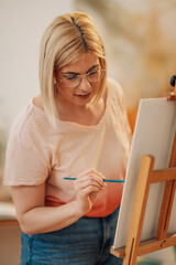 Portrait of focused young artist painting on easel at creative atelier