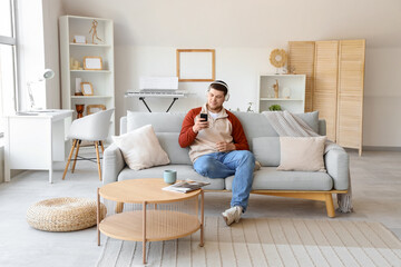 Young bearded man in headphones with mobile phone listening to music on sofa at home