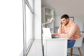 Young bearded man with laptop putting on earphones at home