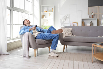 Young tattooed man in earphones with mobile phone listening to music on armchair at home