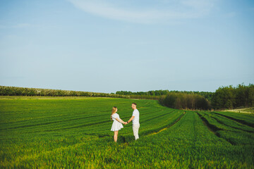 Pregnant couple hugging in a green spring field. Expectant parents in the park of white flowering trees. A romantic couple expecting a baby. A walk through a green field