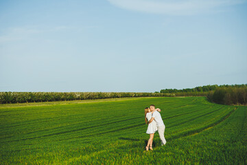 Pregnant couple hugging in a green spring field. Expectant parents in the park of white flowering trees. A romantic couple expecting a baby. A walk through a green field