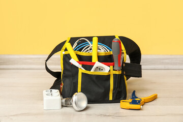 Bag with electrician's tools, extension cord and light bulb on floor near yellow wall
