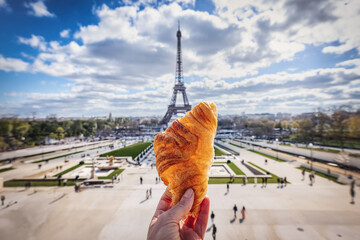 A hand holding a french Croissant in front of the Eiffel Tower in Paris as travel concept for France