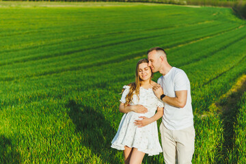 Pregnant couple hugging in a green spring field. Expectant parents in the park of white flowering trees. A romantic couple expecting a baby. A walk through a green field