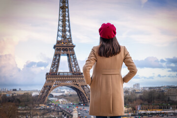 A elegant woman with a red beret hat looks at the Eiffel Tower of Paris, France