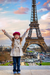 A happy, cute girl with a trench coat and a beret hat in front of the Eiffel Tower in Paris, France, during sunset time