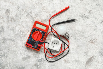 Multimeter, light bulb and electric socket on white grunge background