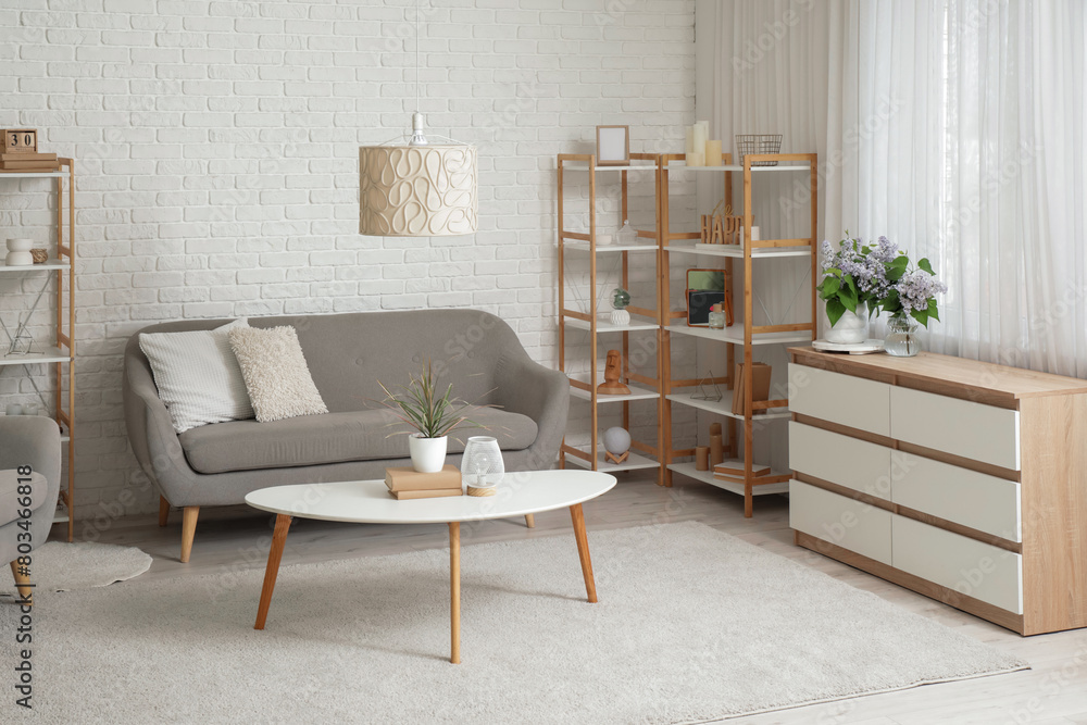 Sticker vases with flowers on chest of drawers, sofa, table and shelving unit near white brick wall