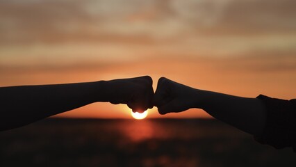 Hands clashing fists brofist at sunset. Bump clash of two fists. Confrontation competition. Gesture of giving respect approval. Teamwork friendship partnership working together at agricultural farm.