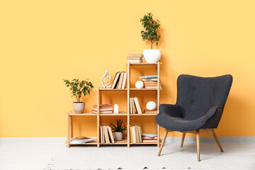 Bookcase with books and houseplants near black armchair in living room