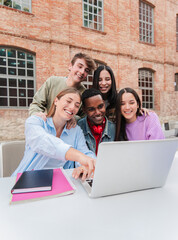 Vertical. Group of multiracial teenage students smiling using a laptop to search information for...