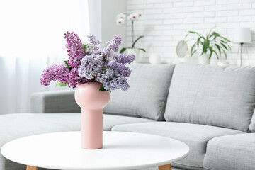 Stylish interior of living room with bouquet of lilacs branches on coffee table near sofa