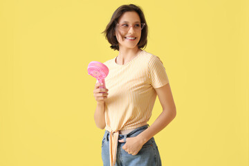 Young woman with pink small electric fan on yellow background