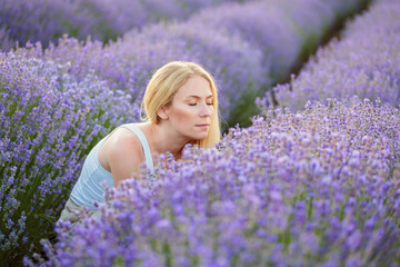 Lavender field. Young attractive woman with blond hair walking between rows of lavender flowers,...