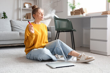 Young woman smoking disposable electronic cigarette on floor at home