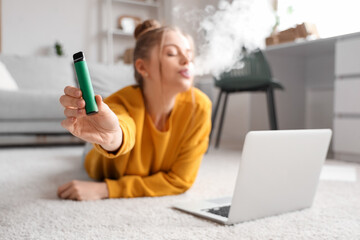 Young woman smoking disposable electronic cigarette on floor at home