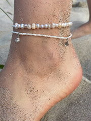 Close-Up of Woman's Foot with Sand and Elegant Pearl Anklet.
