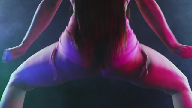 Hot woman dancing, shaking, twerking buttocks in multicolor light, dark studio background. Modern dance - twerk. 
