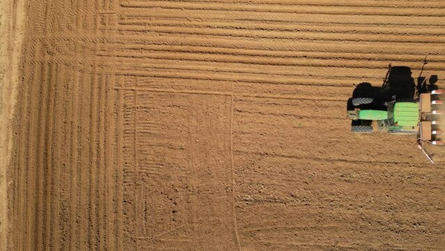 Aerial tracking high angle shot of tractor seeding a field with a seed drill in the mountains on a sunny spring day. Planter towed by a machine along a rural farmland. Ecologic farming concept.
